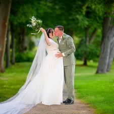 Braut und Bräutigam küssen sich romantisch in einem grünen Park.