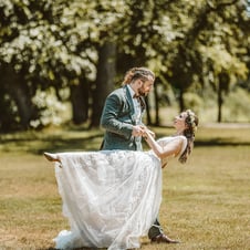 Ein Paar tanzt in einem grünen Park, das Brautkleid schimmert im Sonnenlicht.