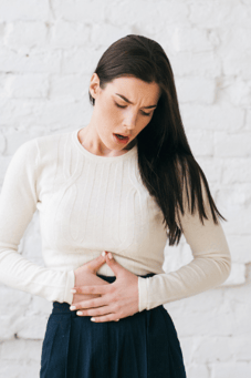 Mulher com a mão no estômago indicando dor abdominal e prisão de ventre