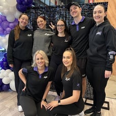 The Anytime Fitness Chermside team with Carly from SweetAz Co. posing in front of the black shimmer wall and purple and white