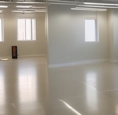 A roughly constructed wall made of various types of wooden panels, each differently colored and textured. Some parts are painted yellow, while darker brown and black wood panels are interspersed. The wall is supported by two vertical beams, and the floor underneath appears to be dirty and unfinished. The ceiling also has an unfinished look with exposed elements.