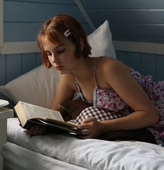 Una mujer con un vestido rosa está leyendo un libro acostada en una cama