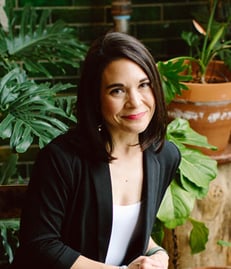 Woman looking at camera, posing in front of plants. 