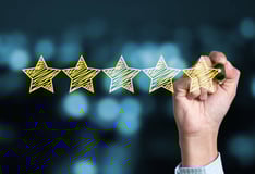 Hand completing a five-star review, signifying top online reputation and customer satisfaction.