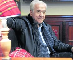 a man in a black jacket and tie dye on a chair