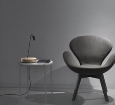 Lámpara de sobremesa con base circular junto a butaca en ambiente de lectura moderno