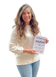 pretty woman in jeans and a white sweater with long brown hair and a smile, holding a book