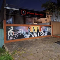 Fachada externa noturna do Studio Brothers com mural de notas musicais em Porto Alegre
