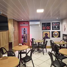 Lounge da cafeteria com mesas e pôsteres de rock no Studio Brothers em Porto Alegre
