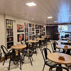 Área da cafeteria com mesas cadeiras e pôsteres de rock no Studio Brothers em Porto Alegre