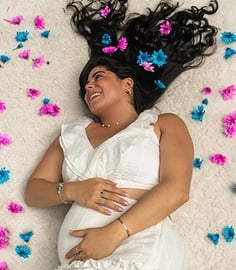 Revelación de género, mujer acostada entre flores rosas y azules, mostrando felicidad y emoción.