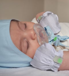 Bebê dormindo de luvas e touca.
