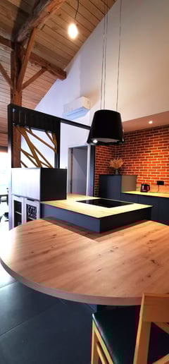 Cuisine vert foncée avec table en bois centrale posée sur îlot avec hotte suspendue. Plan compact