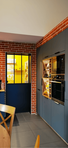 Cuisine vert foncé avec portes anti trace de doigts. Porte cellier style atelier, mur en briques.