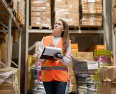 a woman in a safety vest holding a clipboard in a warehouse