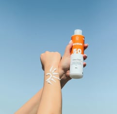 An arm with sunscreen cream and the other hand holding a sunscreen bottle