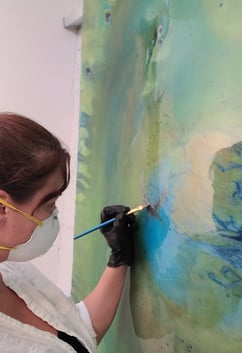 a woman in a mask and gloves is painting Parrot Spirit