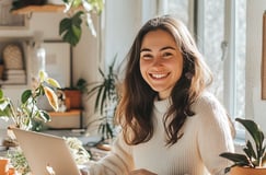 Mujer joven sonríe frente a su laptop en un espacio luminoso, representa emprendimientos digital en un ambiente inspirador.