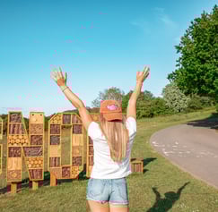Person wearing a Big Food Festival cap standing in front of a large wooden 'GNOLL' sign with arms ra