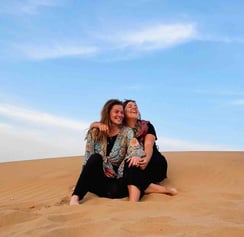 Eva et Manon, two travelers sitting in the Jaisalmer desert, surrounded by golden dunes at sunset.