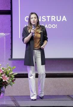 uma mulher em pé encima de um palco, em frente a um projetor de imagens com um microfone