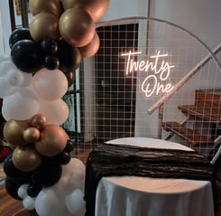 Circle mesh backdrop with a gold Twenty One neon sign with a black, gold and white balloon garland, Redlands.