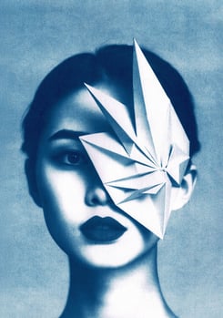 Close-up of a woman with blue-toned skin, dark lips, and a geometric paper structure covering her ri