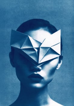 Close-up of a woman with a dark lip color, wearing a white geometric paper mask covering her eyes an