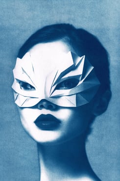 Portrait of a woman with bold lipstick, wearing a geometric paper mask resembling abstract feathers,