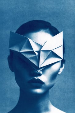 Close-up of a woman with a dark lip color, wearing a white geometric paper mask covering her eyes an