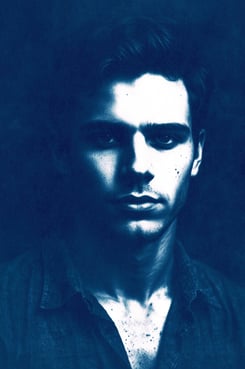 Close-up portrait of a young man with a serious expression, defined features, and short wavy dark ha