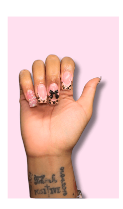 a person's hand with a tattoo on their wrist. Nails are done with a animal print tip and bow accent