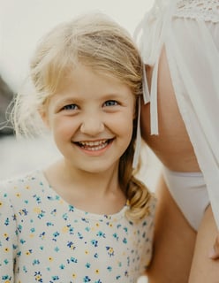 Petite fille souriante qui écoute le ventre rond de sa maman – séance photo grossesse dans le Gard