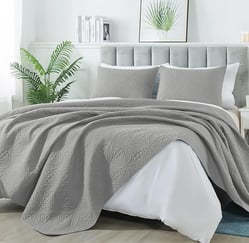 a bed with a grey bedspread and a plant