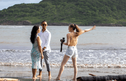 a man and woman standing on a beach while Solana photographs