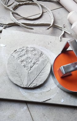a person using a circular tile cutter to make a clay tile printed with thing from natures