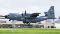 US Air Force Hurricane Hunter plane taking off with ground just below plane and control tower in back ground.