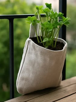 Tote bag suspendu à une rambarde de balcon, recyclé en pot de culture avec du céleri.