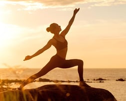 Uma mulher praticando yoga ao ar livre, em um cenário inspirador com o pôr do sol ao fundo. 