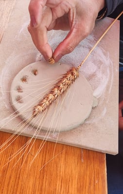 a person pressing a wheat ear into clay