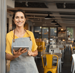 A happy restaurant owner standing with a tablet POS system ready to greet customers.