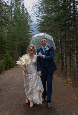 Bride and groom walking down a path in the woods in Banff