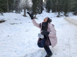 a woman in a pink coat and black boots is throwing snowballs