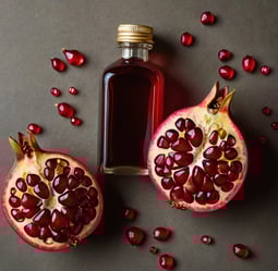 a bottle with red pomegranate oil on a table am two pomegranate