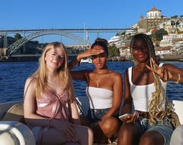 Three girls posing for a photo on the Endure speedboat with Dom Luís I Bridge in the background