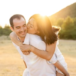 Playful couple at sunset in Provence — she rides on his back and kisses his cheek in soft light