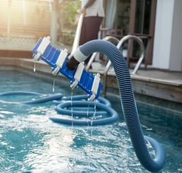 Close-up of a blue pool vacuum head and hose draining water after use during routine maintenance.