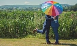 a gay couple on the day of the civil partnership kissing under a rainbow umbrella.