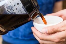 a person is pouring a cup of coffee into a cup