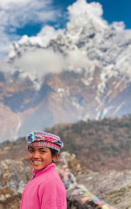 Portrait of a young Nepali girl with a snow-covered peak in the background.